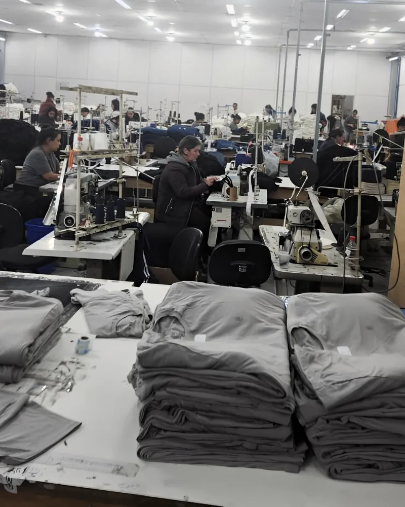 Linha de costura com camisetas dobradas na mesa e costureiras nas máquinas